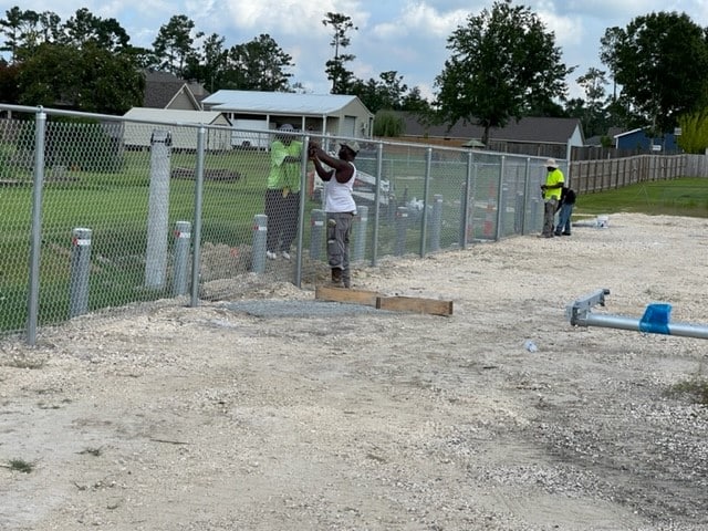 Workers finishing 6-foot fence protecting new drainage ditch at far western portion of parking lot