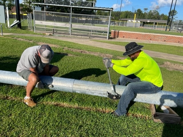 Workers by hand crank light pole that came in two pieces. This will have brackets added and then fixtures attached before a crane is used to place over concrete pole bases